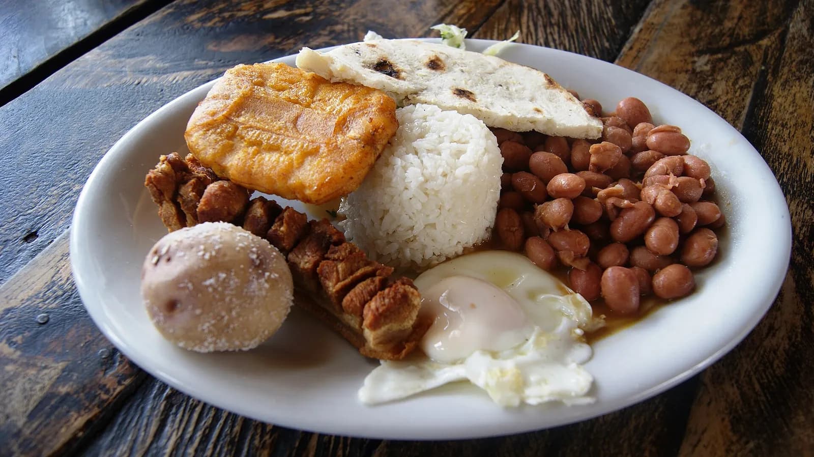 Bandeja paisa servida en un plato sobre una mesa de madera